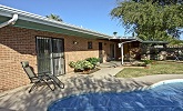 brick single story house with a blue-tiled pool and outdoor furniture, side view of home with grass yard and plants, tucson arizona by owner vacation pet friendly rental home