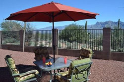 patio/deck with table and chairs for 4 with green seat cushions and large red umbrella open to cover table in shade, beautiful mountain view in the background, mental fence with stone (?) columns, pet friendly vacation home for rent in tucson